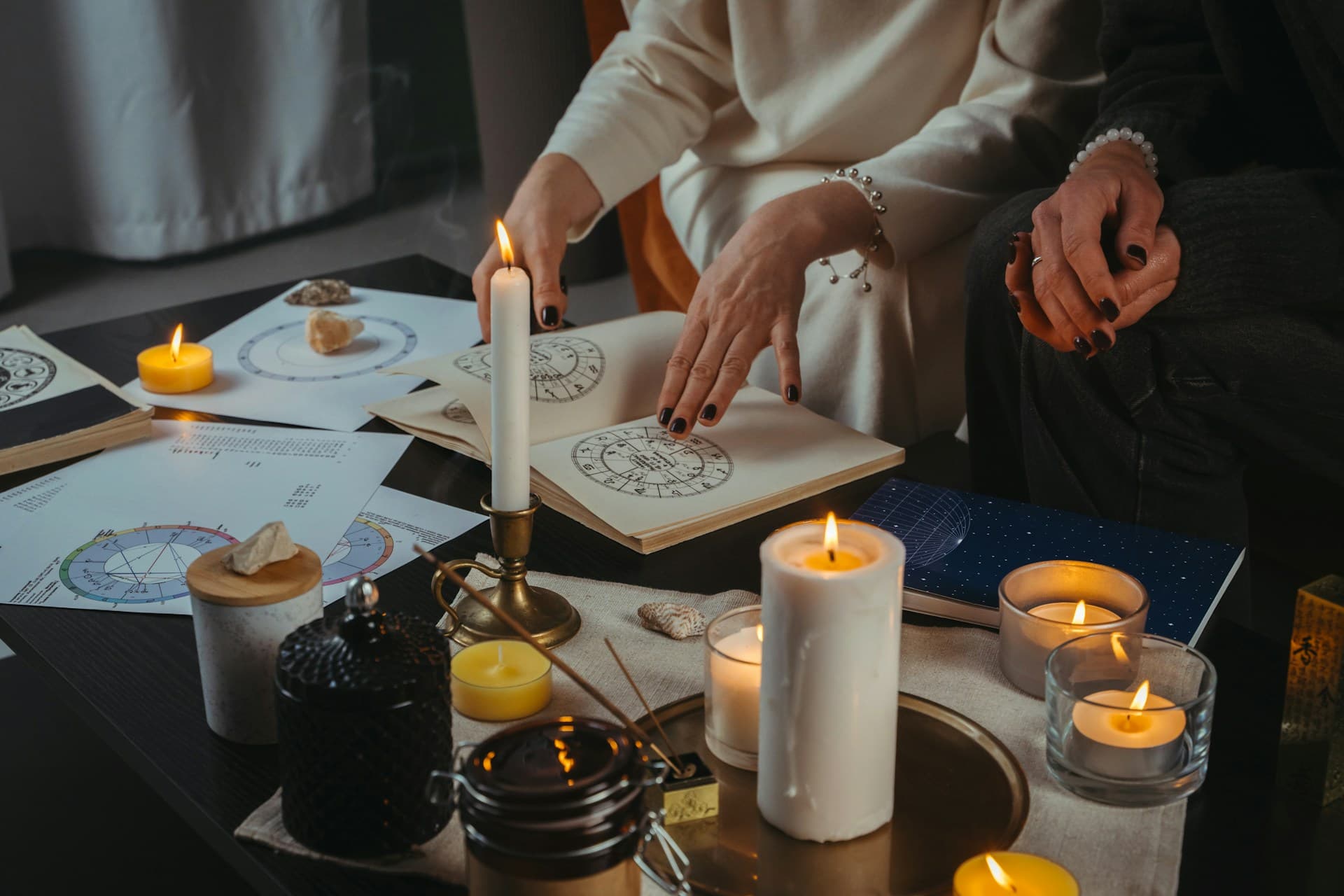 Two individuals studying astrological charts surrounded by candles, crystals, and spiritual items, symbolizing an astrological consultation setting.