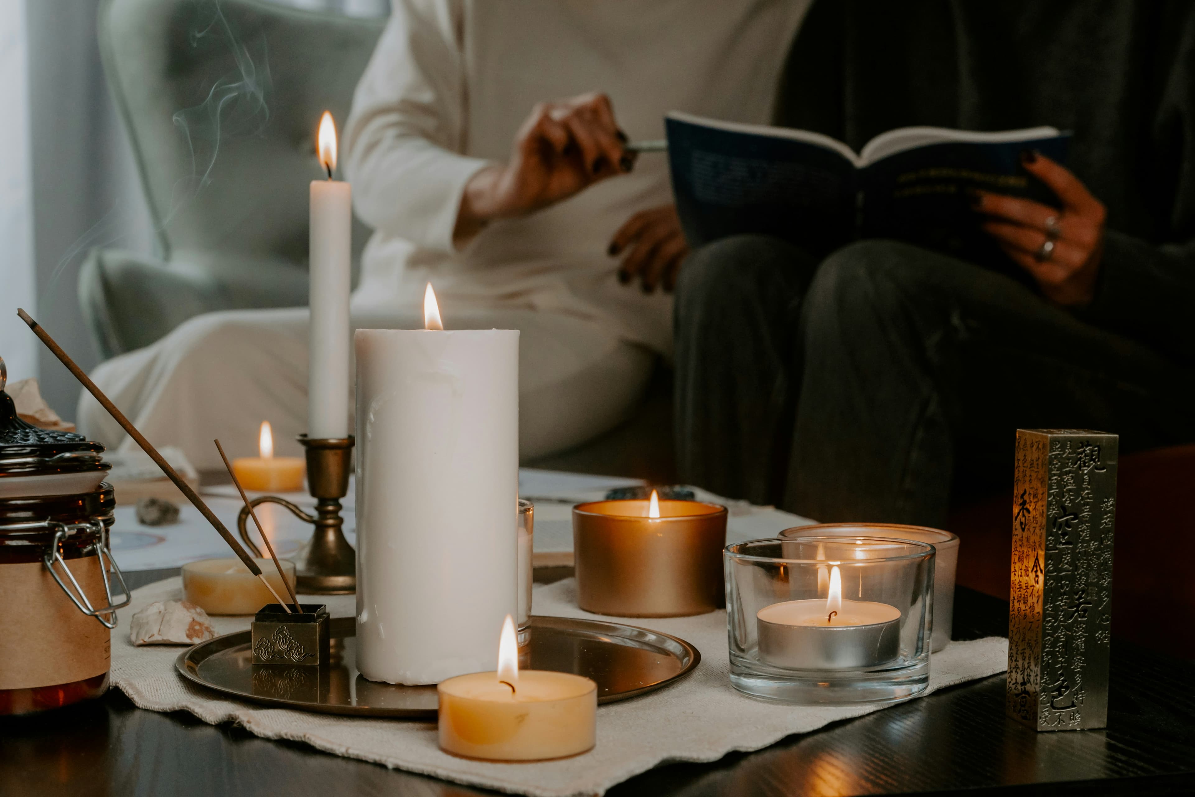 Lit candles and incense on a table with people reading in the background, representing ritual design.