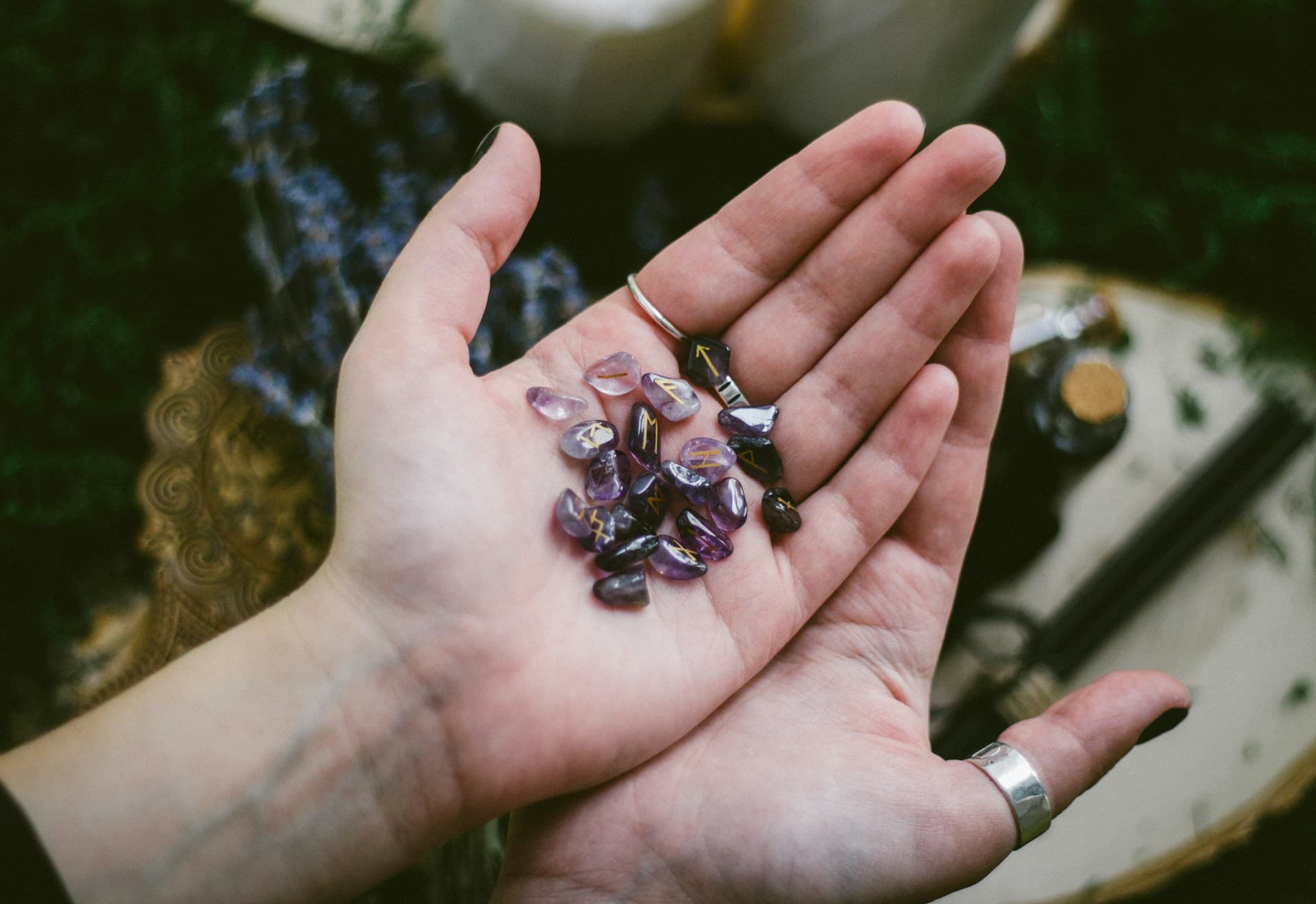 Hands holding crystals and beads over a book with astrological symbols, representing wisdom unlocking.