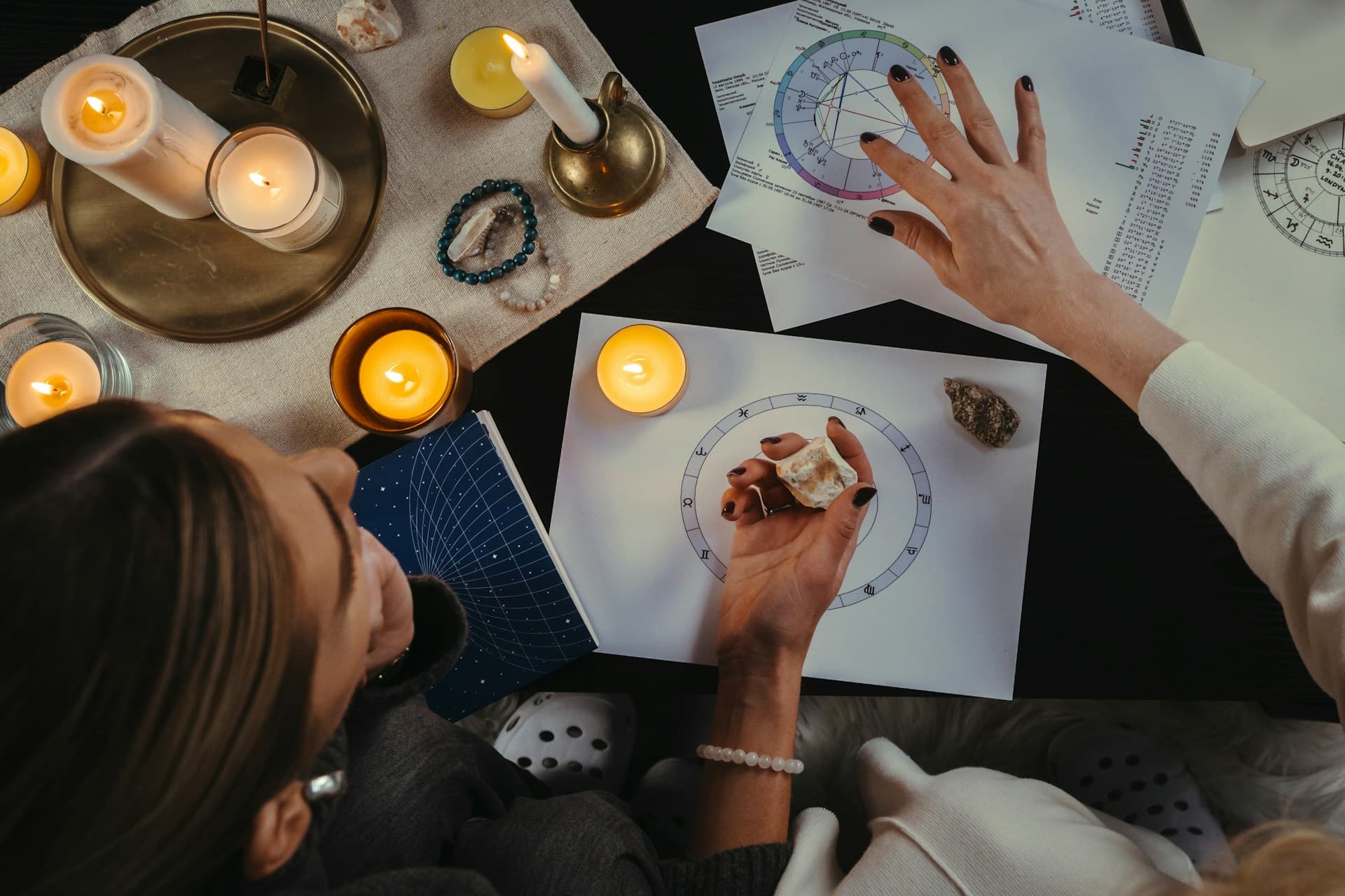 Two people studying a natal chart in a dimly lit room, table filled with candles and papers with astrological symbols